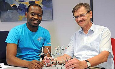 Blaise Kimbadi Lombe mit seinem Doktorvater Gerhard Bringmann. Das Molekülmodell auf dem Tisch zeigt, wie komplex die Naturstoffe gebaut sind, die der Doktorand erforscht. (Foto: Robert Emmerich)