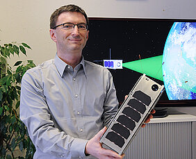 Hakan Kayal mit einem Modell das Nanosatelliten, der voraussichtlich 2019 im Rahmen der SONATE-Mission in den Orbit geschickt werden soll. (Foto: Robert Emmerich)