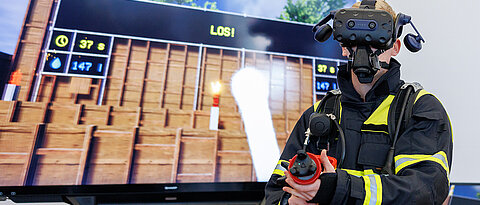 Alexander Schweigert, Lehrkraft an der staatlichen Feuerwehrschule Würzburg, demonstriert mit VR-Brille und einem Hohlstrahlrohr mit VR-Technik das virtuelle Training zur Innenbrandbekämpfung. 
