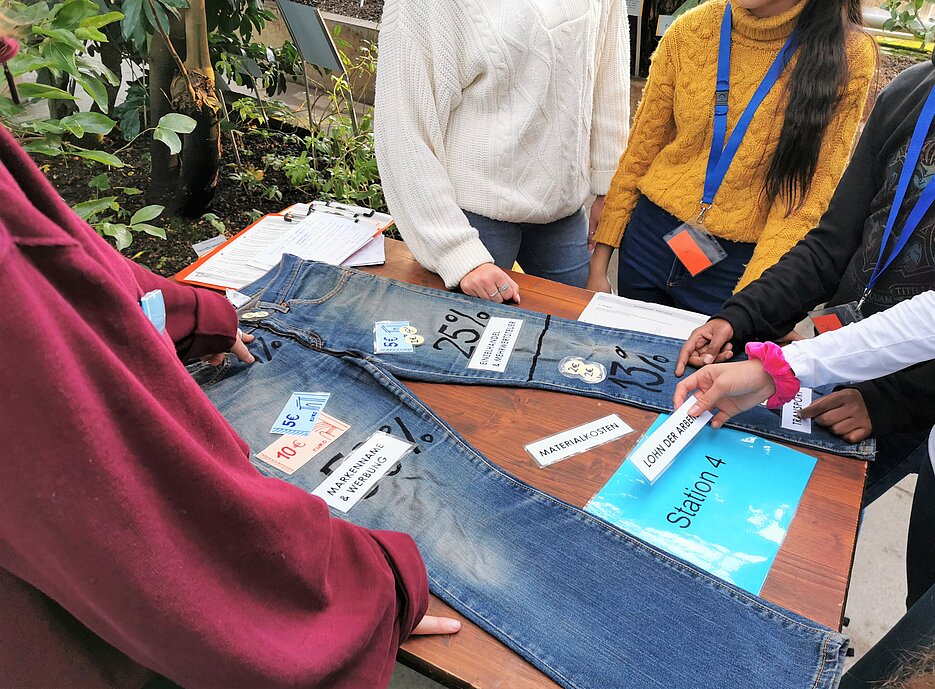 Auf dem Foto erarbeiten Studierende mit Schülerinnen und Schülern die Wertschöpfungskette einer Jeans.