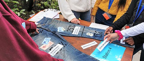 Auf dem Foto erarbeiten Studierende mit Schülerinnen und Schülern die Wertschöpfungskette einer Jeans.