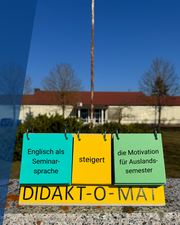 Aufsteller mit Text "Englisch als Seminarsprache steigert die Motivation für Auslandsaufenthalte" steht vor einem Unigebäude.