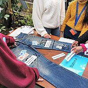 Auf dem Foto erarbeiten Studierende mit Schüler:innen die Wertschöpfungskette einer Jeans.