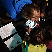 Kinder spielen auf einem Tablet, neben ihnen liegen Dokumente.