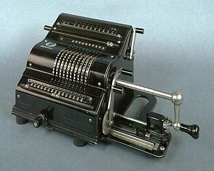 Hier sieht man eine Rechenmaschine. In ihrer Optik ähnelt sie einer Schreibmaschine. Anstelle von Buchstaben, gibt es Ziffern von 1-10 und das 10 mal. Schließlich kann man 15-stellige Zahlen errechnen.