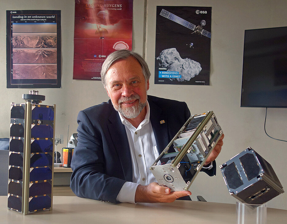 Klaus Schilling with the satellites that have accompanied his professional life. UWE and NetSat in the foreground; on the posters in the background HUYGENS and ROSETTA, which were realised during his work in industry.