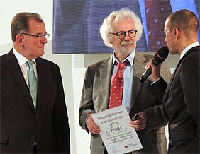 Bildunterschrift Jürgen Tautz (Mitte) ist der Gewinner des Unterfränkischen Inklusionspreises in der Kategorie „Bildung und Erziehung“. Bezirktagspräsident Erwin Dotzel (l.) hat ihm auf der Ufra in Schweinfurt die Urkunden überreicht. Rechts im Bi