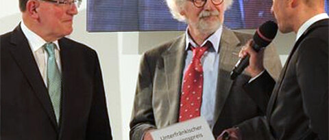 Bildunterschrift Jürgen Tautz (Mitte) ist der Gewinner des Unterfränkischen Inklusionspreises in der Kategorie „Bildung und Erziehung“. Bezirktagspräsident Erwin Dotzel (l.) hat ihm auf der Ufra in Schweinfurt die Urkunden überreicht. Rechts im Bi