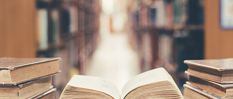 Old book in library with open textbook, stack piles of literature text archive on reading desk, and blur aisle of bookshelves in school study class room background for education learning concept