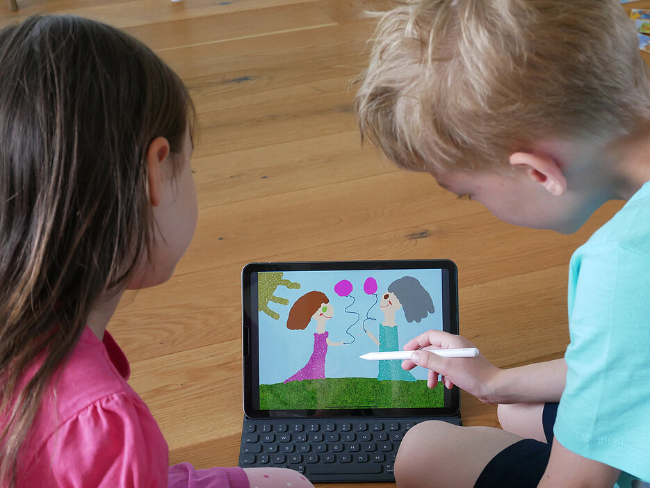Zwei Grundschulkinder erstellen ein digitales Bilderbuch auf einem Tablet.
