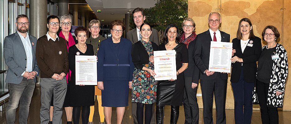 Mitstreiterinnen und Mitstreiter auf dem erfolgreichen Weg zum Selbsthilfefreundlichen Uniklinikum Würzburg (UKW) sowie Gratulanten (v. l.): Christian Holzinger (Aktivbüro derStadt Würzburg), Andreas Selig (Paritätischer Wohlfahrtsverband Bezirksverband Unterfranken), Dorothea Eirich und Dr. Renate Fiedler (Selbsthilfevertreterinnen des UKW), Kathrin Speck (Paritätischer Wohlfahrtsverband Bezirksverband Unterfranken), Barbara Stamm(Landtagspräsidentin a.D.), Christian Schuchardt (Oberbürgermeister der Stadt Würzburg), Dr. Hülya Düber (Sozialreferentin der Stadt Würzburg), Gabriele Nelkenstock (externe Selbsthilfebeauftragte des UKW), Antje Liesener (Koordinatorin des Netzwerks „Selbsthilfefreundlichkeitund Patientenorientierung“), Dr. Gerhard Schwarzmann (Leiter der Stabsstelle Qualitätsmanagement des UKW), Susanne Wundling (Aktivbüro der Stadt Würzburg) und Susanne Just (Stabsstelle Kommunikation des UKW). 