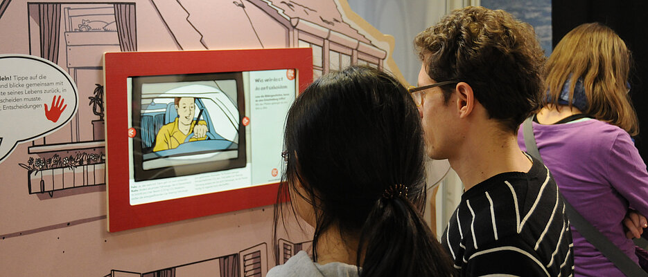 Zwei Personen vor einem Bildschirm in einer Ausstellung