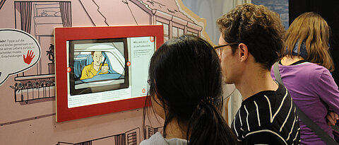 Zwei Personen vor einem Bildschirm in einer Ausstellung