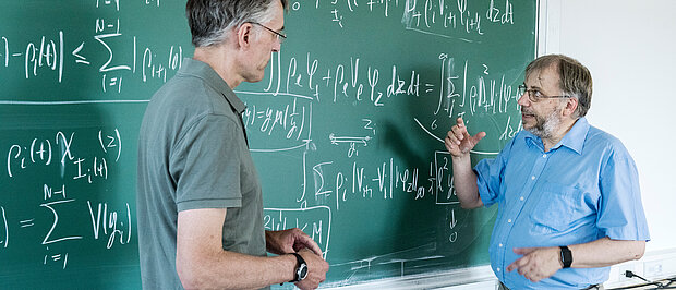 Forscher diskutieren vor Tafel mit mathematischen Formeln