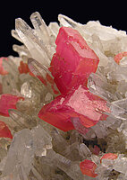 Kleine, bis 1,5 cm breite himbeerrote Rhodochrositkristalle vergesellschaftet mit durchsichtigen Quarzkristallen. Ursache für die rosa Farbe ist Mangan