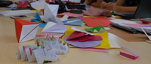 Gefaltetes und buntes Papier auf einem Tisch zur Darstellung der Mathematik des Papierfaltens