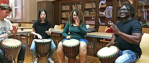 Students performing african percussion on djembe drums.