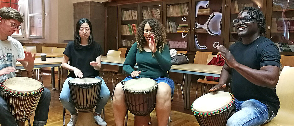 Students performing african percussion on djembe drums.