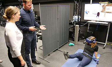 Professor Marc Latoschik und seine Mitarbeiterin Andrea Bartl (mit VR-Brille) erklären, wie Virtuelle Realität das Reha-Training nach einer Knie-Operation effektiver machen kann.