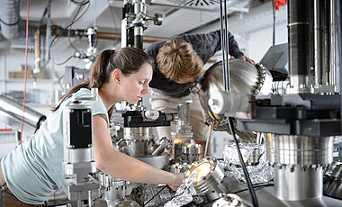 Forschung in Claessens Labor: Lisa Mündlein und Philipp Schütz arbeiten an einer Ultrahochvakuum-Apparatur: Sie haben einen nur wenige Atomlagen dünnen Film hergestellt, den sie für weitere Untersuchungen im Vakuum bewegen und neu positionieren. (Foto: Daniel Peter)