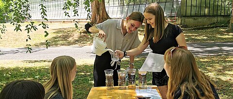 Anhand eines Filterversuchs setzten sich Schüler:innen eines Gymnasiums an der ersten Station des Workshops mit der Wasserspeicherkapazität verschiedener Böden auseinander. Das Foto zeigt die Durchführung des Filterversuchs im Botanischen Garten unter Anleitung der verantwortlichen Studentin. (Foto: Anna Dävel)