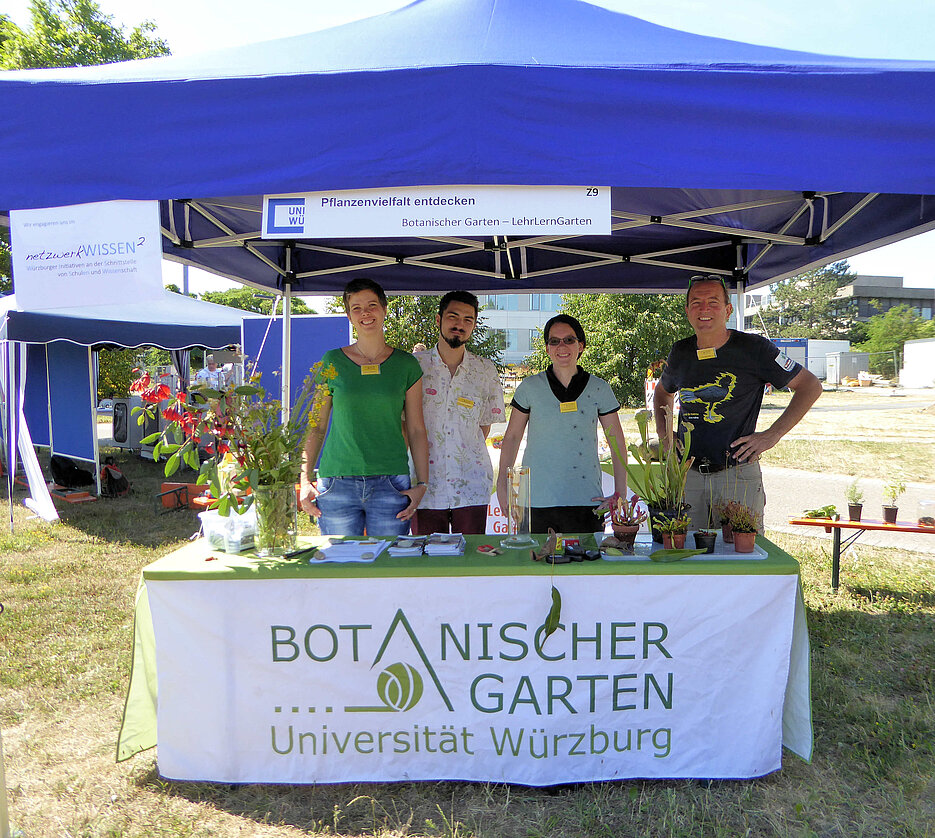 2 Studierende, Koordinatorin Dr. Kerstin Bissinger und Kustos Dr. Gerd Vogg am Stand des Botanischen Gartens, auf dem Tisch steht ein Blumenstraus und verschiedene fleischfressende Pflanzen