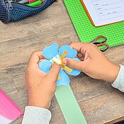 Ein Kind basteltet ein eigenes Blütenmodell aus Papier.