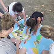 Das Foto zeigt Studierende und Schüler:innen bei einem Workshop zur Welternährung. Sie ordnen Bildkarten verschiedener Früchte auf einer Weltkarte ihren Herkunftsregionen zu.