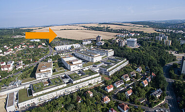 Das Schrägluftbild verdeutlicht die Lage des Erweiterungsgeländes (Pfeil) oberhalb des Parkplatzes des Uniklinikums Würzburg. Im Vordergrund ist das Doppelzentrum für Operative und Innere Medizin mit seinen vier Bettenhäusern zu erkennen. 