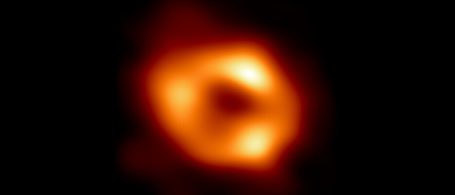 Erstes Bild des Schwarzen Lochs im Zentrum der Milchstraße. Es zeigt glühendes Gas, das um das Schwarze Loch kreist und eine verräterische Signatur trägt: eine dunkle zentrale Region, die von einer hellen ringförmigen Struktur umgeben ist. Die Aufnahme fängt das Licht ein, das durch die starke Schwerkraft des Schwarzen Lochs gebeugt wird.