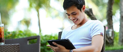 Junger Mann sieht gut gelaunt auf ein iPad