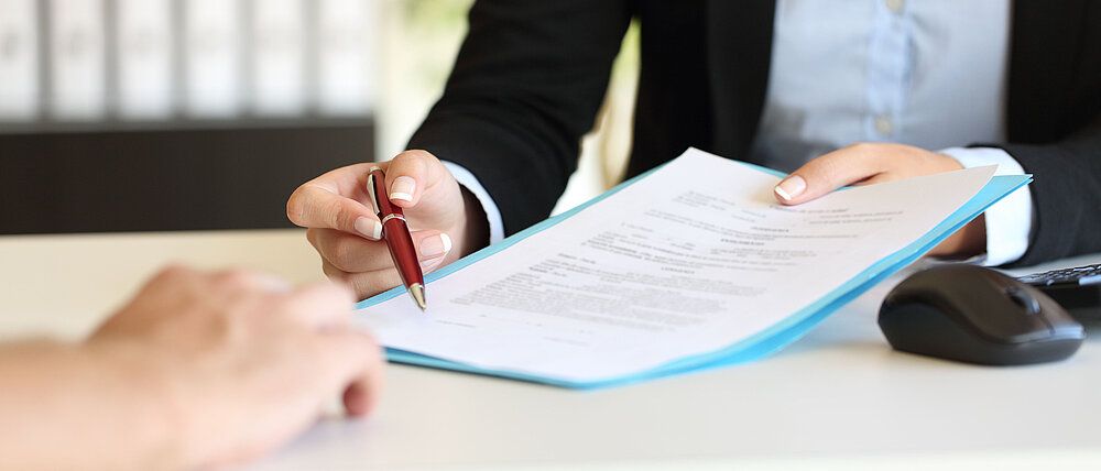 Close up of an executive hands holding a pen and indicating where to sign a contract at office