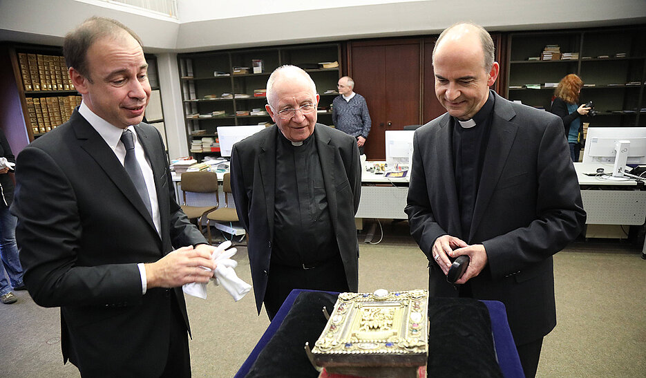 Hans-Günter Schmidt (links), Leiter der Universitätsbibliothek, präsentiert Bischof Franz Jung (rechts) und Domprobst Weihbischof Ulrich Boom das Kiliansevangeliar.