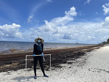Prof. Laura Otto am Strand in Mexiko mit Maske, da die Algen stinken