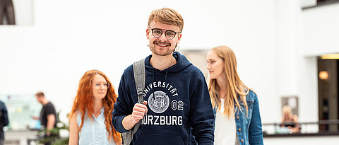 Person schreibt mit Stift, Das Logo der Universität ist verschwommen im Hintegrund zu sehen.