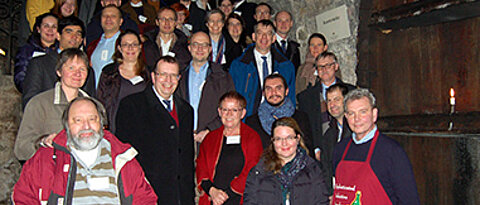 Gruppenbild der neuen Professorinnen und Professoren auf einer Treppe im Staatlichen Hofkeller. In der ersten Reihe von rechts nach links: Jochen Gummersbach vom Hofkeller,  Hanna Kounev vom Welcome Center der Uni,  Bürgermeisterin Marion Schäfer-Blake 