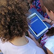 Eine Gruppe Schüler:innen stehen um ein Tablet herum.