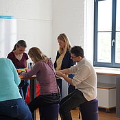 Fünf Personen stehen an einem Tisch und schreiben.