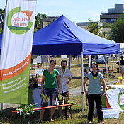 Stand des LehrLernGartens. Links im Bild die Fahne mit LLG Logo, zwei Studierende und Dr. Kerstin Bissinger warten auf die Besucher.