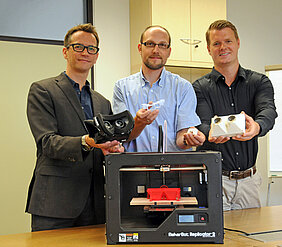 Matthias Funken, Frank Steinicke und Bernhard Ludewig mit dem 3D-Drucker „Replicator 2“ und einigen Objekten, die an der Uni Würzburg damit bereits gedruckt worden sind. (Foto: Robert Emmerich)
