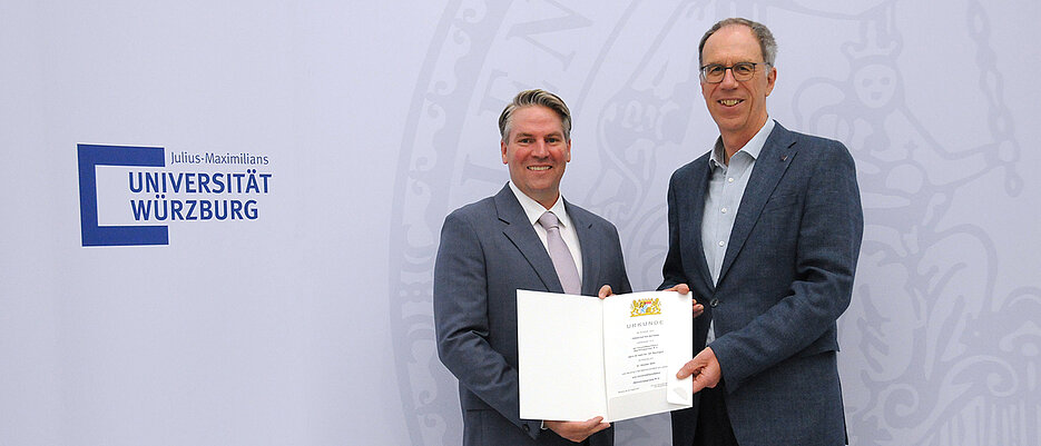 Universitätspräsident Paul Pauli überreicht Jan Baumgart die Ernennungsurkunde.