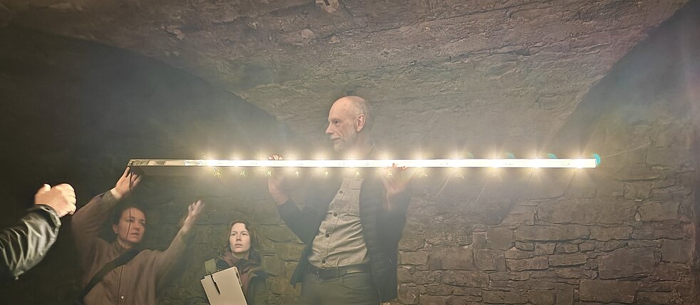 Person mit Lichtschiene in den Händen unter dem Gewölbe des Weinkellers