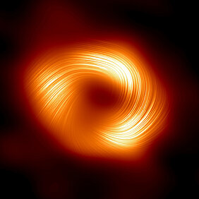 Abb. 1:  Die Event Horizon Telescope (EHT)-Kollaboration, die das erste Bild des Schwarzen Lochs im Zentrum der Milchstraße erstellt hat (veröffentlicht im Jahr 2022), präsentiert nun eine neue Darstellung des massereichen Objekts im Zentrum unserer Galaxie, nämlich in polarisiertem Licht. Dies ist das erste Mal, dass Astronomen die Polarisation, eine Signatur von Magnetfeldern, so nahe am Rand von Sagittarius A* messen konnten. Dieses Bild zeigt den polarisierten Blick auf das Schwarze Loch im Zentrum der Milchstraße. Die Linien markieren die Ausrichtung der Polarisation, die mit dem Magnetfeld um den Schatten des Schwarzen Lochs zusammenhängt.
