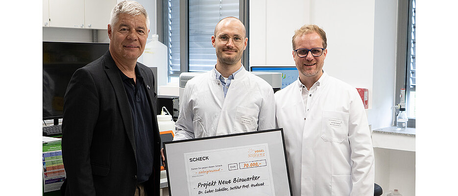 Bei der Scheckübergabe am 06. Juli 2026 am UKW-Lehrstuhl für Zelluläre Immuntherapie (von links): Gunther Schunk (Vogel Stiftung), Lukas Scheller (Universitätsklinikum Würzburg), Michael Hudecek (Universitätsklinikum Würzburg). 
