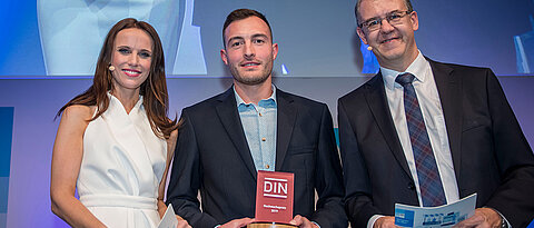 Toni Greif (M.) bei der Preisverleihung in Berlin mit dem DIN-Vorstandsvorsitzenden Christoph Winterhalter und Moderatorin Susanne Schöne.