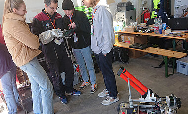 Die Studierenden (v.l.n.r.) Carolin Bösch, Julius Arzberger und Pascal Meyer leiten Analog-Astronaut Simone Paternostro (Zweiter v.r.) beim Test des Handbedienungsgeräts mit Touchscreen mit seinem Handschuh an. 