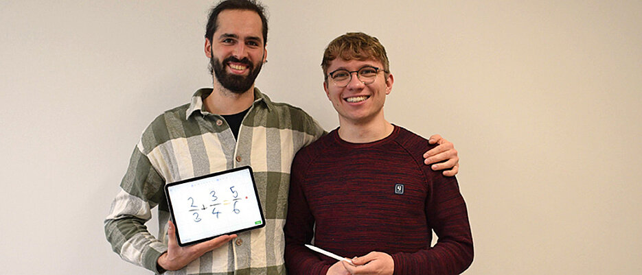 Jakob Seitz und Tobias Lengfeld vom Startup Living-Lines. Auf dem Tablet ist eine falsch gelöste Rechenaufgabe zu sehen; die App zeigt den Fehler mit einem roten Punkt an.