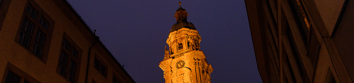 Blick auf den beleuchteten Turm der Neubaukirche. Von dort spielen Musikerinnen und Musiker im Rahmen des Turmblasens am 9. Dezember ab 16:00 Uhr ein kleines Konzert.