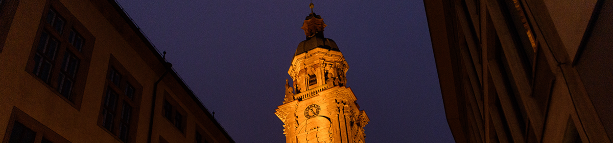 Blick auf den beleuchteten Turm der Neubaukirche. Von dort spielen Musikerinnen und Musiker im Rahmen des Turmblasens am 9. Dezember ab 16:00 Uhr ein kleines Konzert.