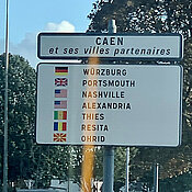 Schild an einer Straße, darauf aufgelistet sind alle Partnerstädte von Caen. Würzburg steht an erster Stelle.